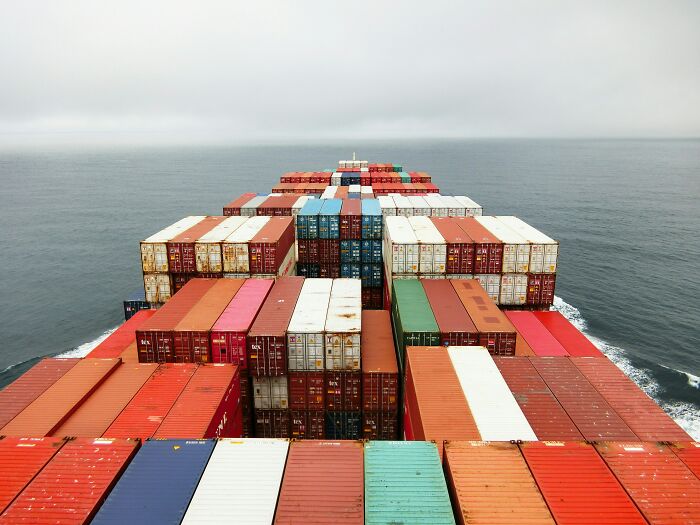 View from cargo ship deck stacked with colorful shipping containers moving across calm ocean.