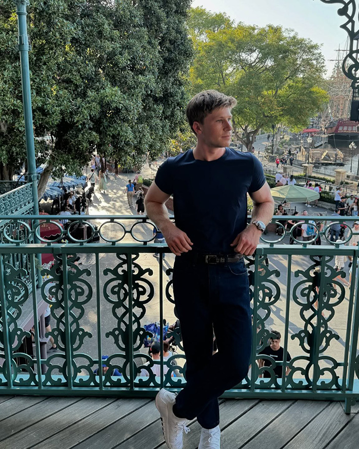 Young man at a popular outdoor Australian restaurant balcony during the day with trees and people in the background.