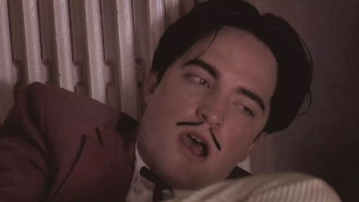 Robert Pattinson in a close-up shot with a drawn-on mustache, recalling a challenging Twilight intimate scene.
