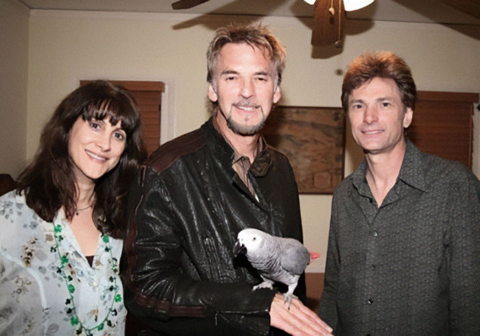 Three people smiling indoors, one holding a parrot, related to American Idol exec and husband police fail case. - 7