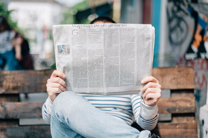Person sitting on a bench reading a newspaper outdoors, illustrating truckers share craziest things seen concept. - 15