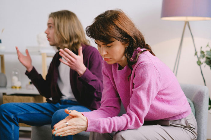 Woman in pink sweater upset while boyfriend&rsquo;s roommate watches Jurassic Park in living room dispute about dinosaurs.