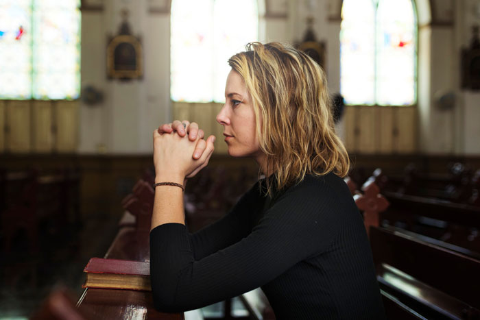 Woman in black shirt sitting in church pew, deep in thought, representing disbelief in dinosaurs topic.