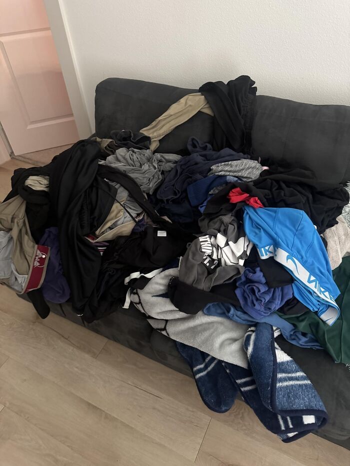 Messy couch covered with a large pile of clothes illustrating bad roommate behavior and common roommate problems.