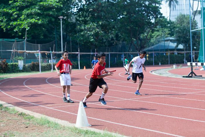Three kids running a relay race on an outdoor track during a sunny day in a sports event for children.