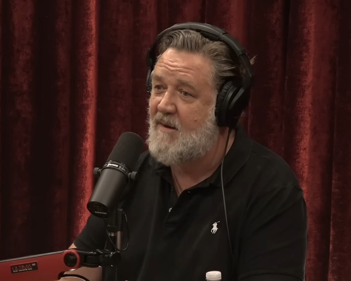 Russell Crowe wearing headphones and black polo shirt speaking into microphone during podcast recording session. Russell Crowe wearing headphones and black polo shirt speaking into microphone during podcast recording session.