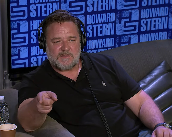Russell Crowe wearing headphones and a black polo, appearing in a Howard Stern studio setting during an interview session. Russell Crowe wearing headphones and a black polo, appearing in a Howard Stern studio setting during an interview session.