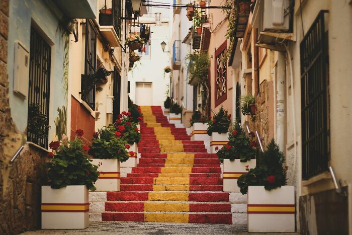 Narrow street with stairs painted in red and yellow, decorated with flowers, reflecting bizarre facts about countries.