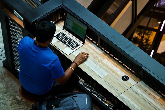 Man in a blue shirt working on a laptop at a modern wooden desk, exploring jobs that make six figures.