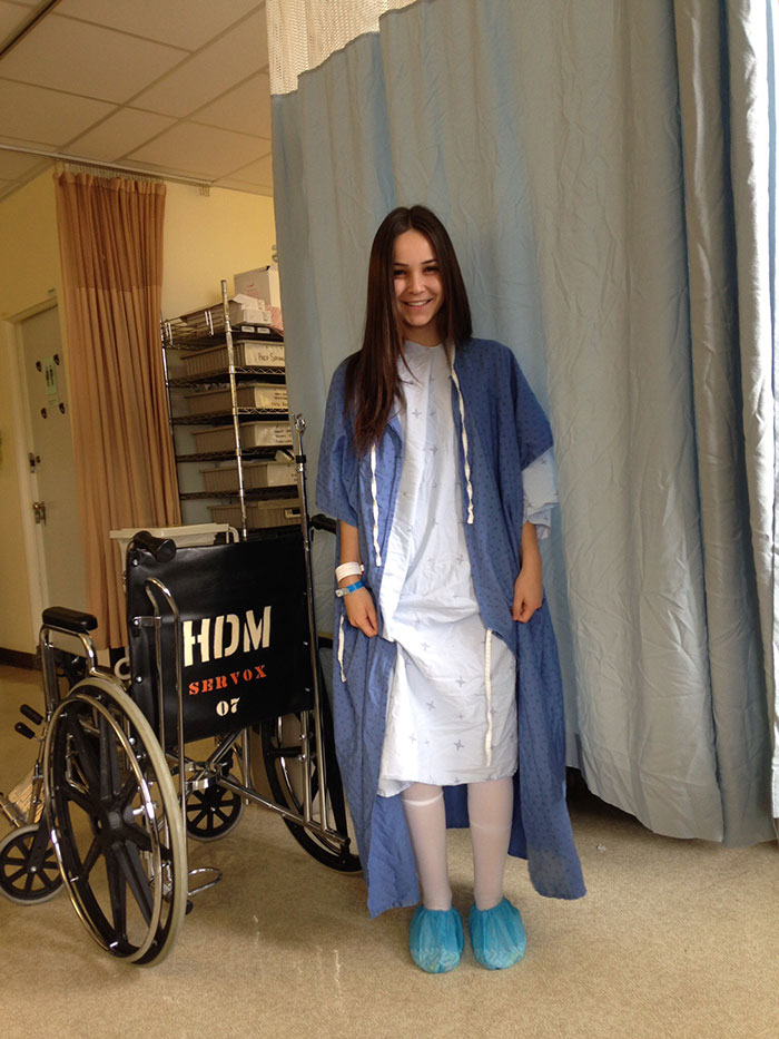 Young woman in hospital gown smiling, showing confidence after years of feeling ashamed of her ostomy bag.