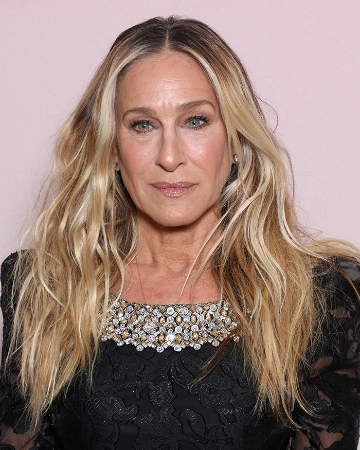 Sarah Jessica Parker with long wavy hair wearing a black embellished top at a public event, showing an awkward expression