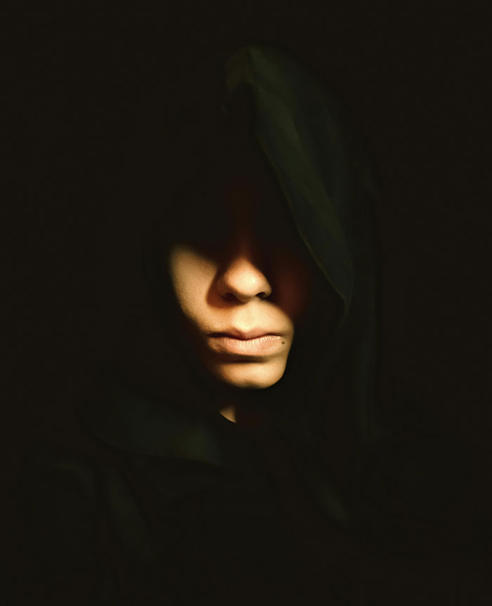 Person wearing a dark hood, face partially lit, creating a mysterious mood related to neighbor tales and moving to the woods.