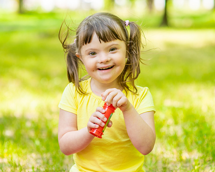 Smiling young girl with Down syndrome playing outdoors on a sunny day, representing gene editing breakthrough.