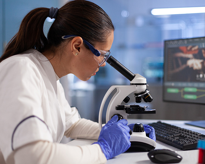 Scientist examining samples through a microscope in a lab, researching gene editing for Down syndrome cure.