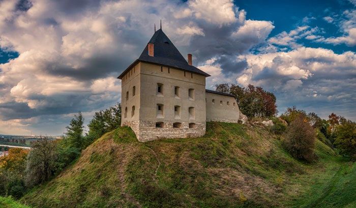 Medieval castle perched on a grassy hill under a dramatic cloudy sky, hinting at a secret chamber beneath the castle.