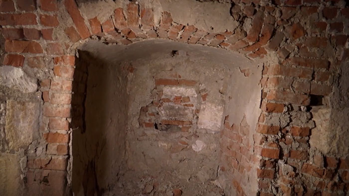 Old brick and stone secret chamber beneath castle walls with arched ceiling and worn mortar in dim lighting.