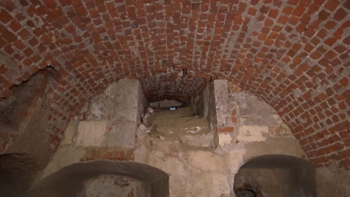 Underground brick vault revealing a secret chamber beneath castle with ancient stone and dirt debris inside.