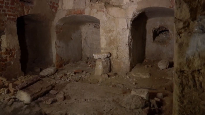 Dimly lit secret chamber beneath castle walls with ancient stone structures and rubble scattered on the floor