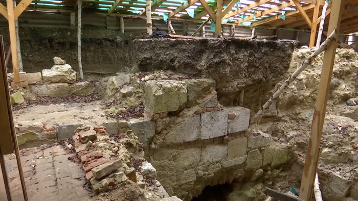 Ruins of an ancient secret chamber beneath castle walls exposed during archaeological excavation under wooden scaffolding.