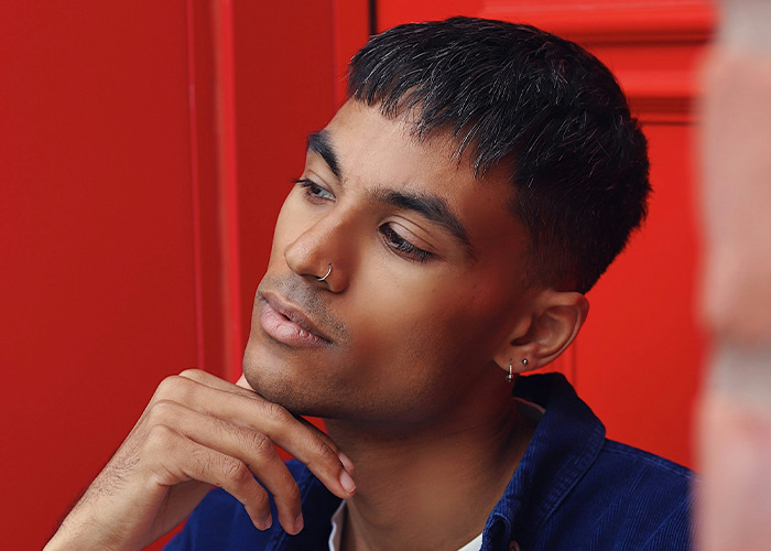 Young man with nose ring and earrings, deep in thought against a red background reflecting on secrets people pray parents never find out. - 17