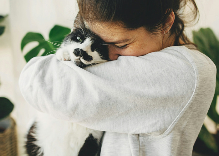Young woman hugging a black and white cat closely, expressing affection and comfort in a cozy setting about secrets. - 18
