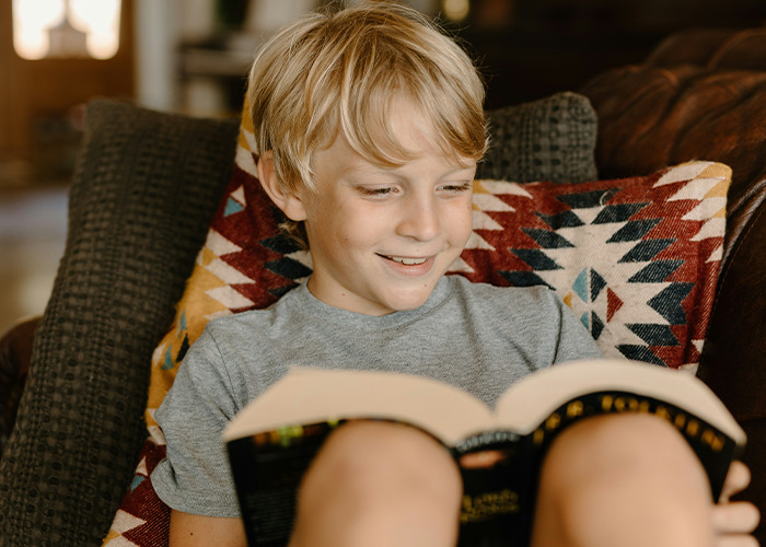 Young boy smiling and reading a book indoors, highlighting secrets people pray their parents never find out. - 7