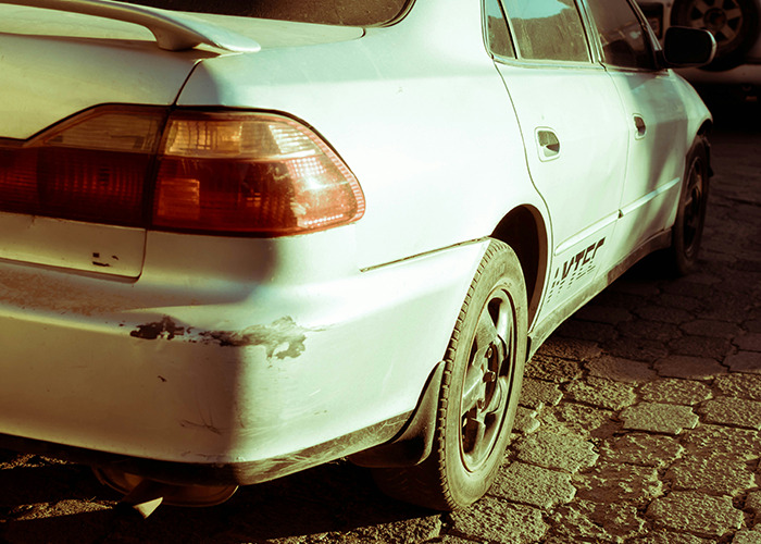 White car with visible scratches on the bumper parked on a paved surface, symbolizing hidden secrets people pray parents never find out - 24