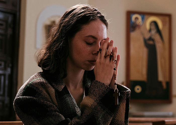 Young woman praying silently in a church, holding a rosary, reflecting on secrets people pray their parents never find out. - 33