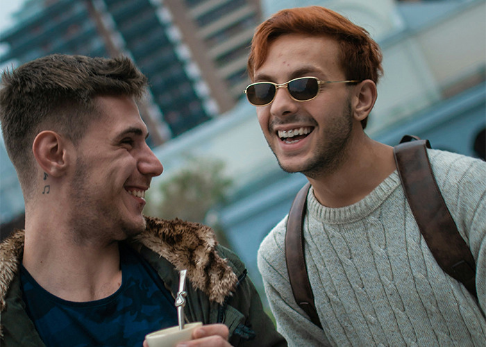 Two young men laughing together outdoors, sharing a moment while holding a beverage, capturing secrets parents never find out. - 12