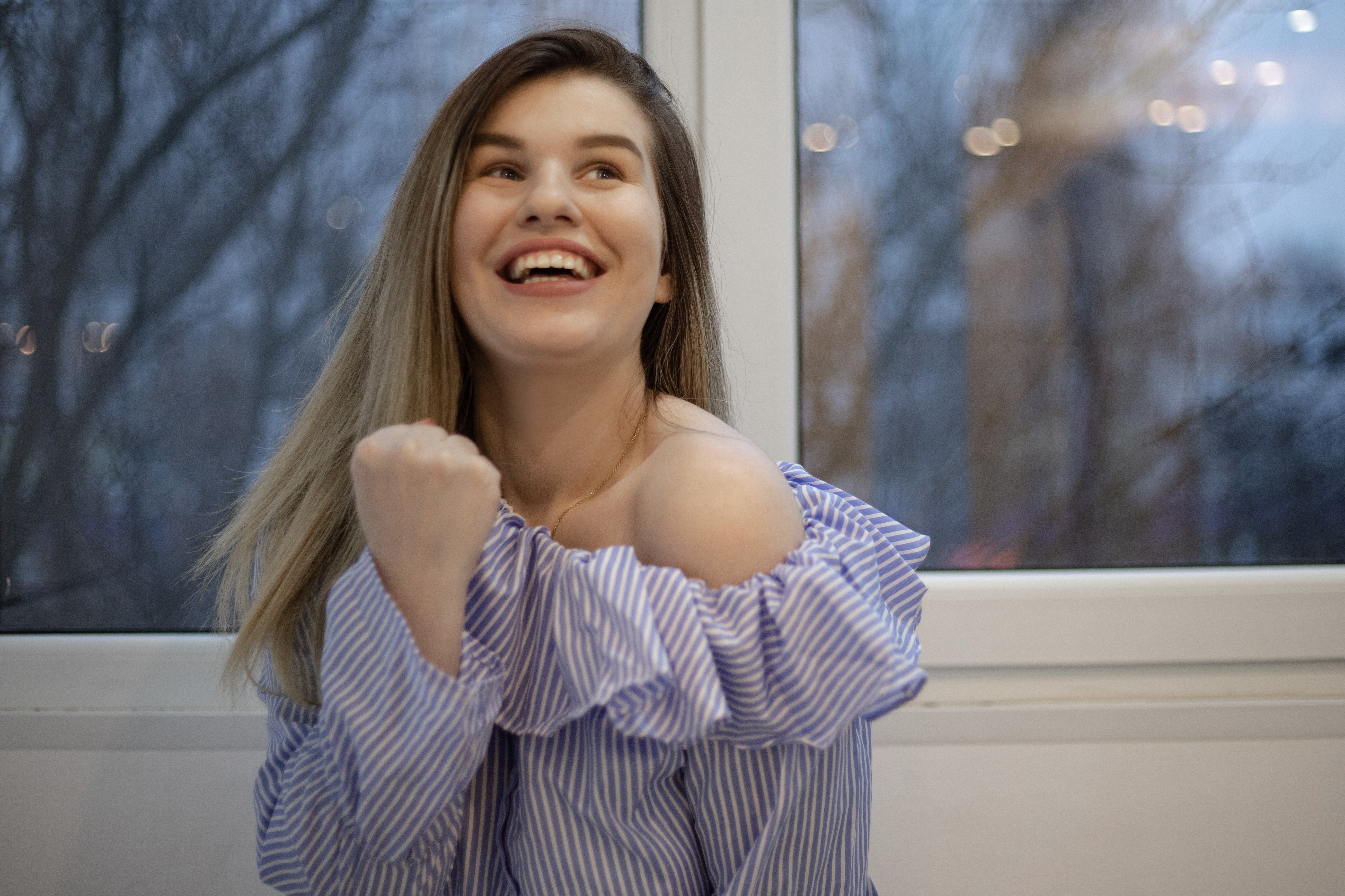 Young woman smiling and celebrating indoors, illustrating a woman putting glitter in roommate&rsquo;s humidifier prank.