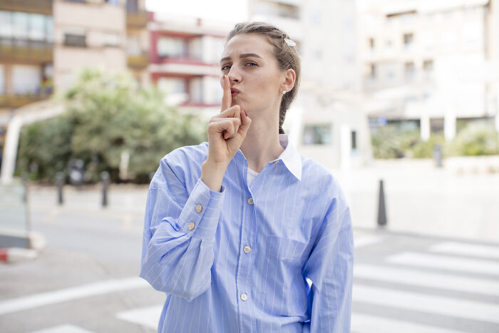 Young woman in a blue shirt making a shushing gesture, symbolizing impactful sentences that changed people’s lives.
