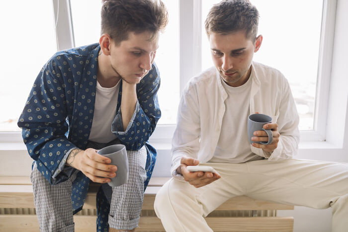 Two young men holding mugs and looking at a phone together, reflecting on life-changing sentences.