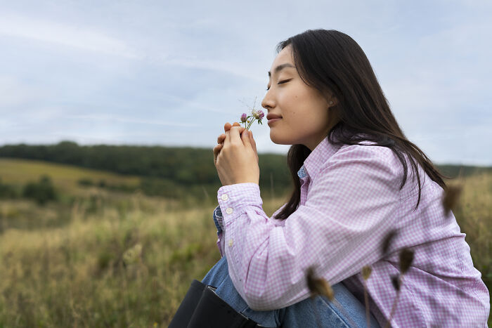 Young woman enjoying nature, sitting in a field, reflecting peacefully with a flower, inspiring life-changing sentences.