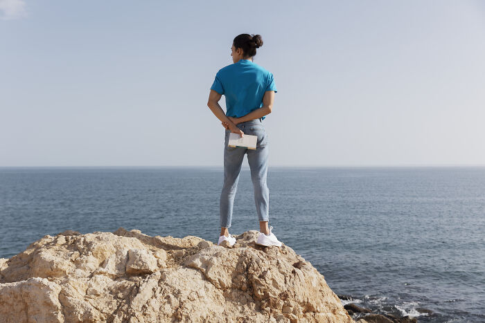Person standing on rocky cliff by the sea holding a notebook, reflecting on life-changing sentences.