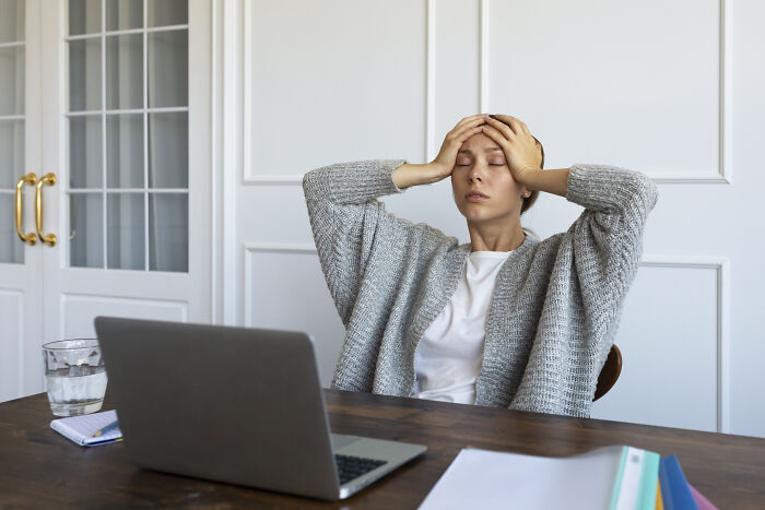 Woman in gray sweater holding her head in frustration while working on laptop about life-changing sentences