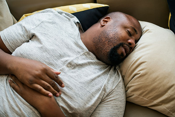 Man lying down with hands on stomach, possibly feeling unwell, illustrating serious medical conditions often dismissed.