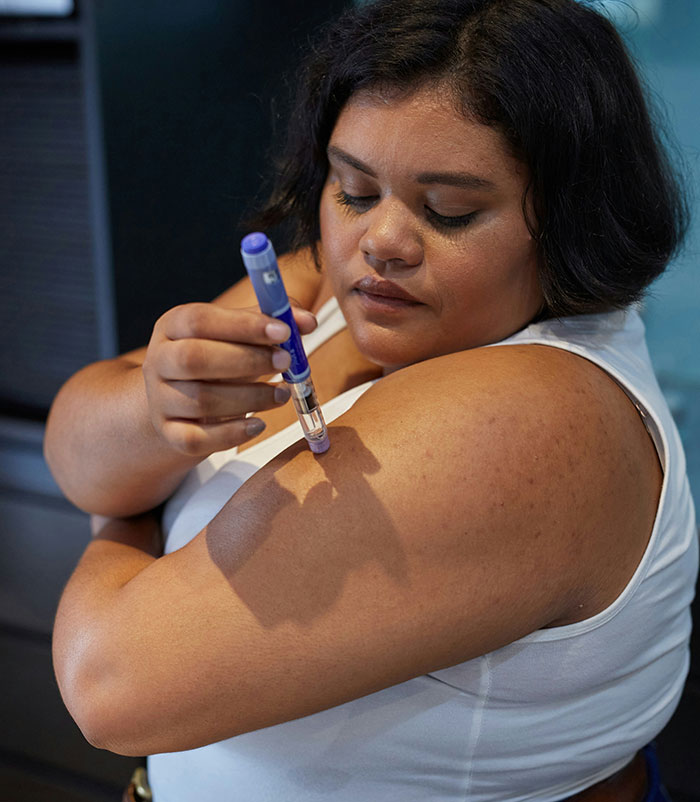 Woman administering an injection to her upper arm representing serious medical conditions often dismissed and delayed diagnosis.
