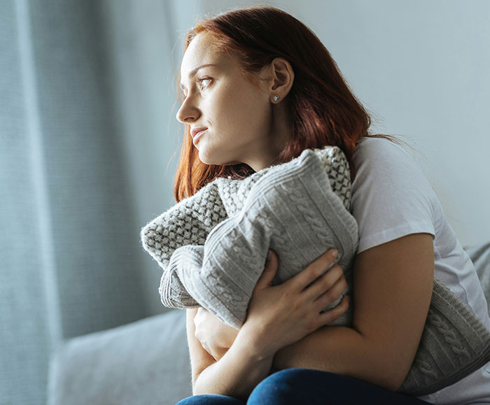 Woman holding a blanket and looking thoughtful, representing the delay in diagnosis of serious medical conditions.