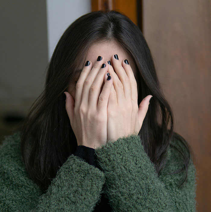 Woman with long dark hair covering her face with hands, representing serious medical conditions often dismissed before diagnosis.