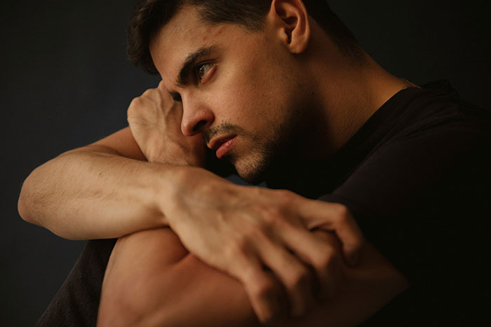 Young man in deep thought with arms wrapped around knees, illustrating serious medical conditions often dismissed.