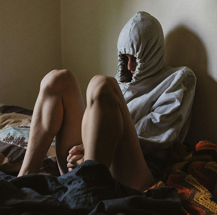Person sitting on bed with hooded sweatshirt pulled tight, representing serious medical conditions often dismissed and delayed diagnosis.