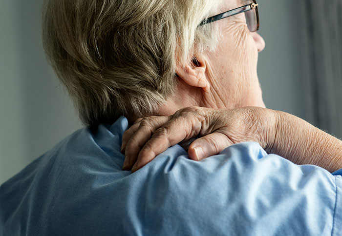 Elderly person in glasses holding neck, portraying discomfort linked to serious medical conditions often dismissed.