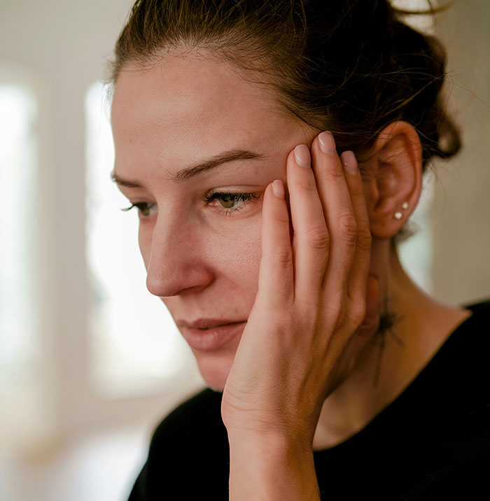 Woman with hand on face looking worried, representing serious medical conditions often dismissed before diagnosis.
