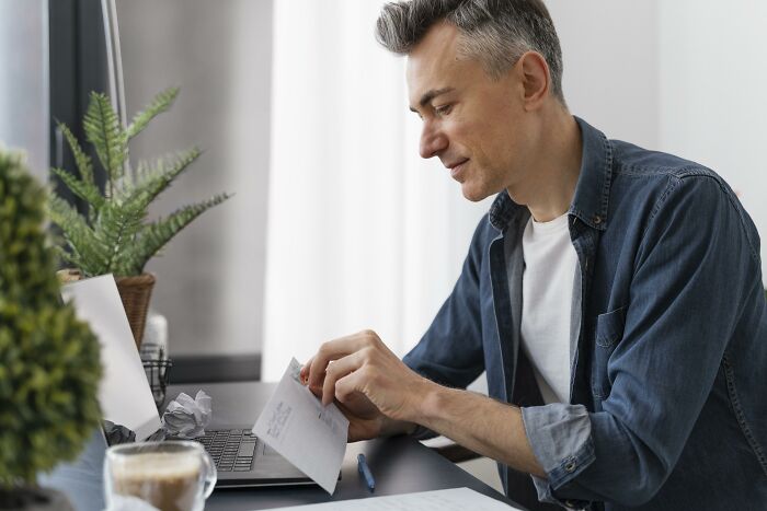 Man reading a letter at a desk with a laptop and plants, illustrating signs you grew up sheltered concept.