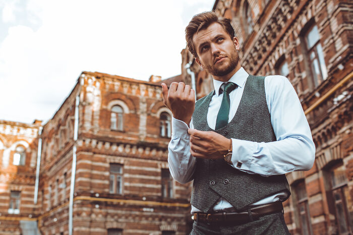 Young man adjusting cufflinks outside old brick building, representing signs you grew up sheltered in appearance and posture.
