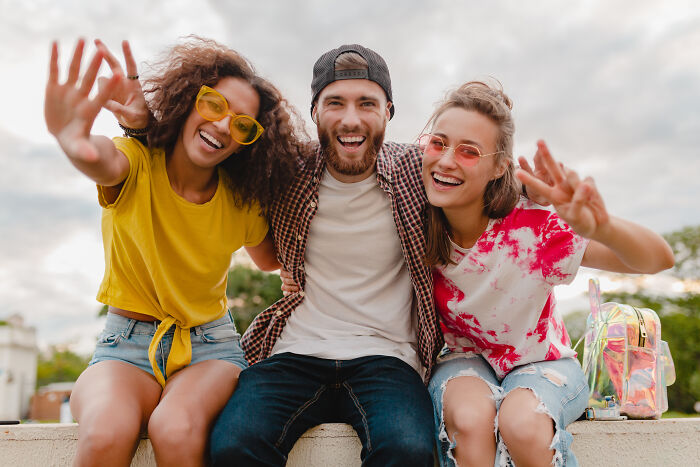 Three friends smiling and posing outdoors, expressing signs they grew up sheltered through their joyful gestures.