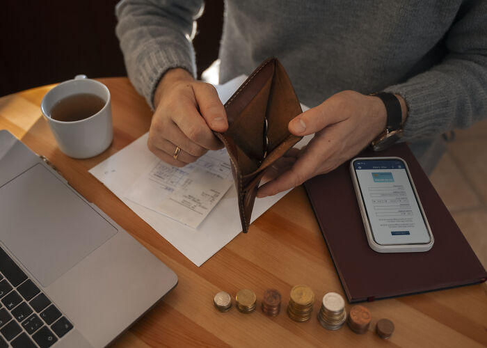 Person holding an empty wallet with coins and a smartphone on a table showing signs they grew up sheltered.