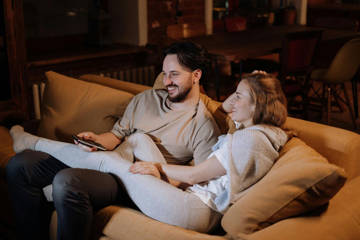 SIL lounges comfortably on the couch smiling while BIL looks ready to manage her kid in a cozy home setting.