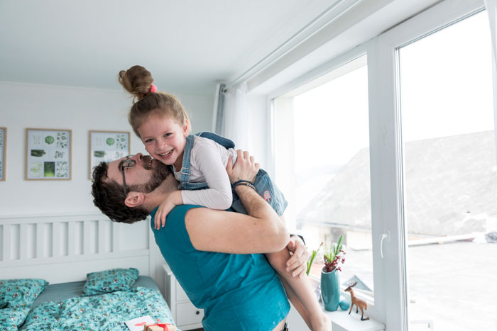 Father lifting daughter joyfully near a window, illustrating family moments and sil pregnancy husband boundaries in a bright bedroom. - 15