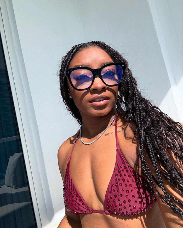Simone Biles wearing large glasses and a maroon studded bikini top, sparking plastic surgery and retirement rumors on vacation.